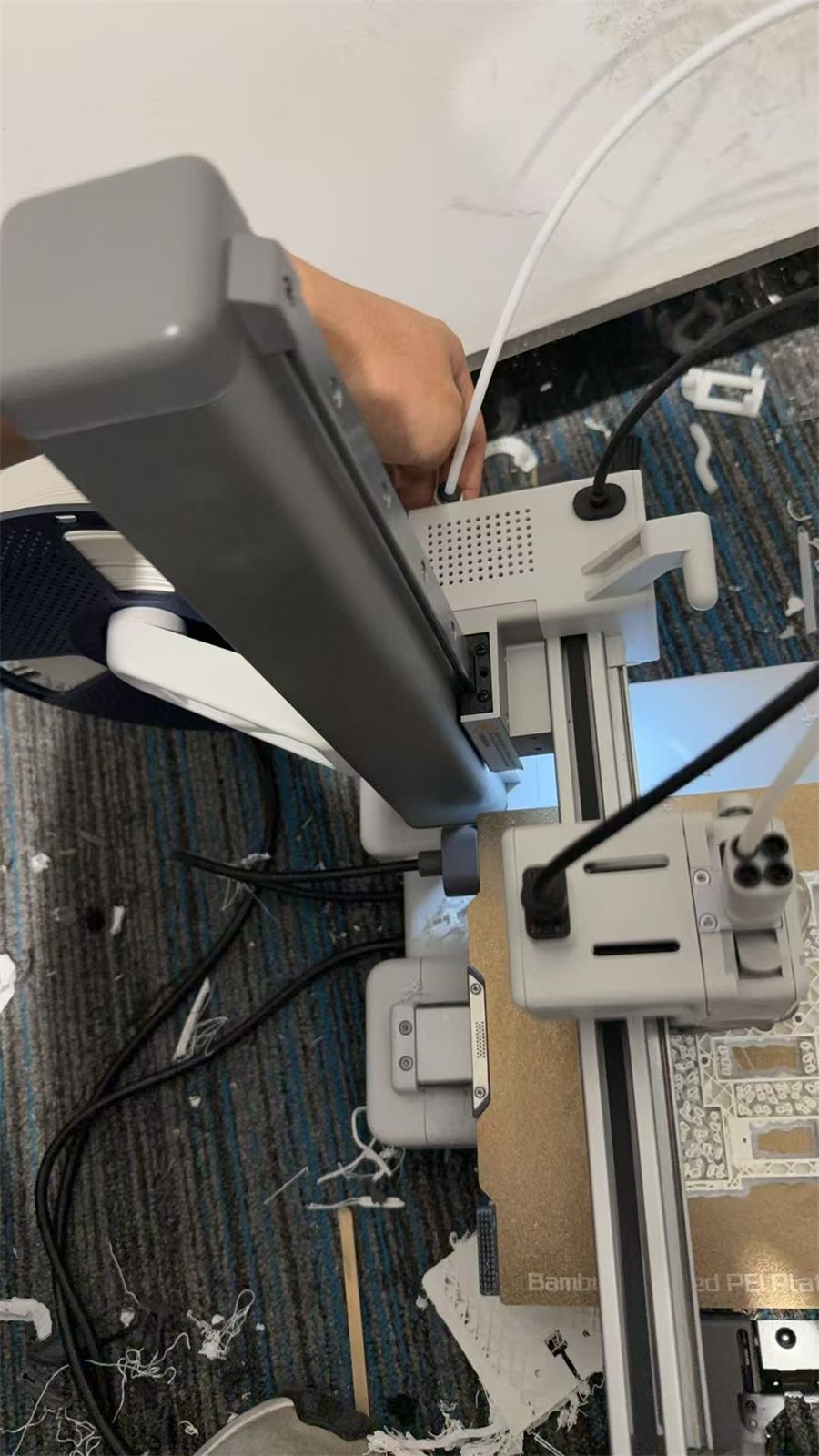 A desktop 3D printer producing a white mechanical part on the lab floor
