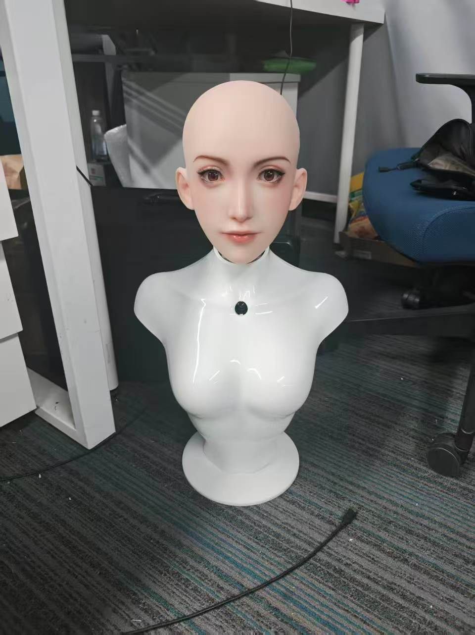 Bald Elva head on a white glossy bust, standing on the lab carpet
