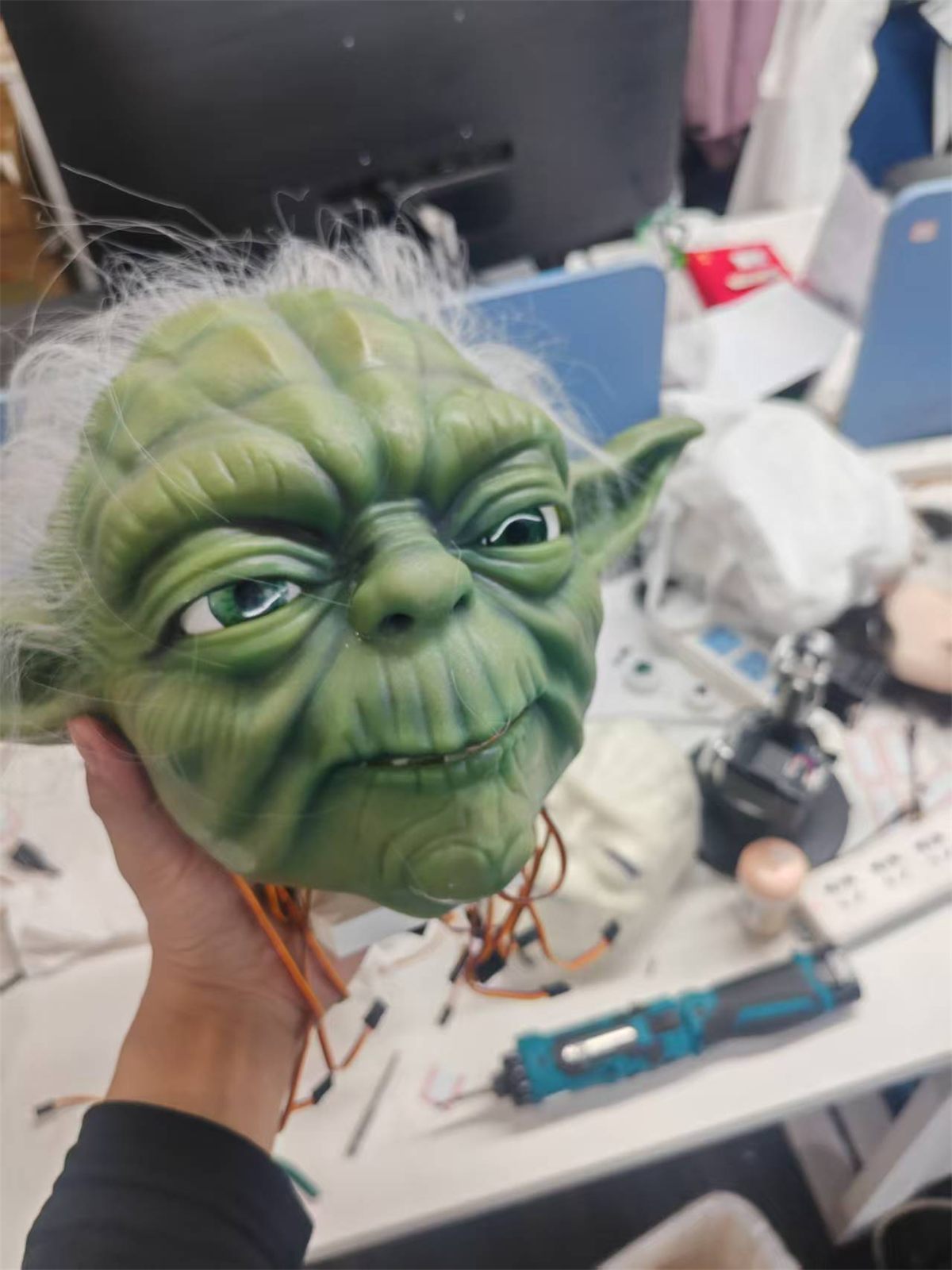 A wired character-study head held above a workshop desk